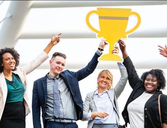 Photo of several office workers holding up and pointing to a trophy while smiling 