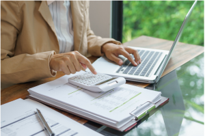 A person using a calculator and laptop to budget